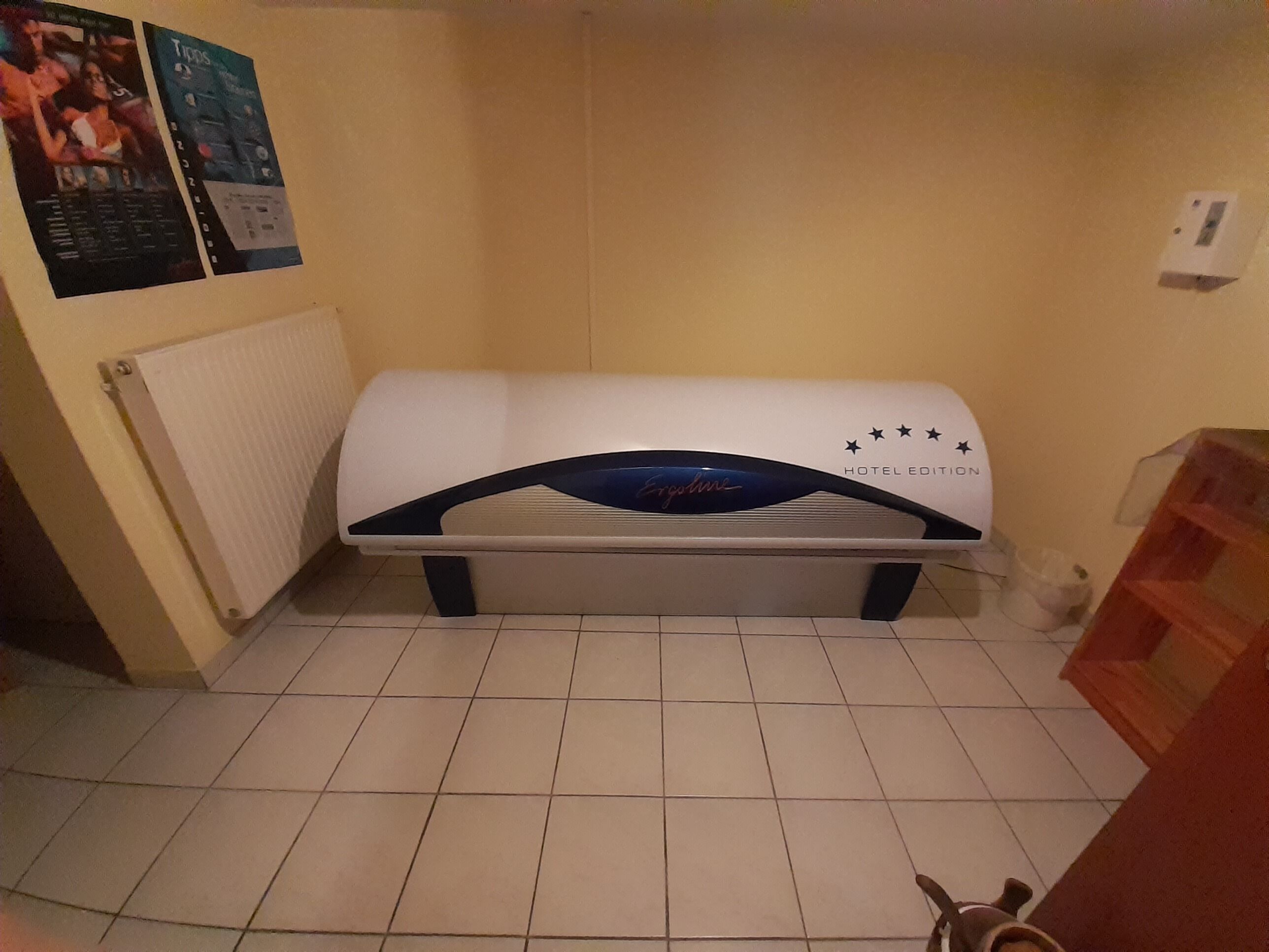 Una habitación de hotel con una cama, un radiador, un cartel en la pared y suelo de baldosas.