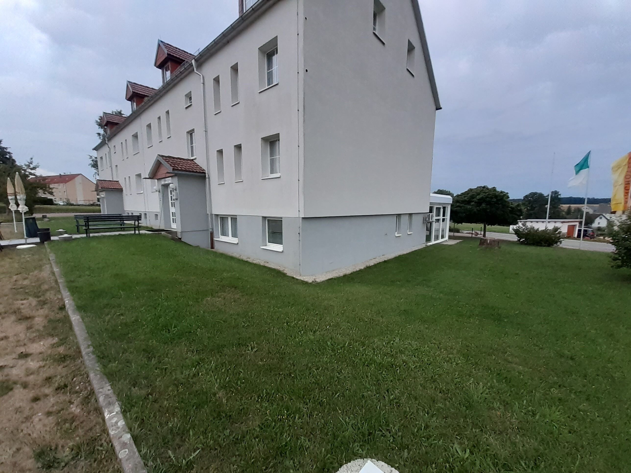 Ein mehrstöckiges Gebäude mit flachem Dach und einem kleinen Garten davor.