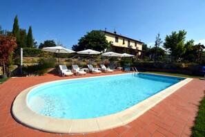 A swimming pool with lounge chairs and umbrellas, surrounded by a brick patio and a building in the background. - VILLA CASALE IL BOSCHETTO - JACUZZI & FITNESS & PLAYGROUND OPEN AIR (Certaldo (Firenze))