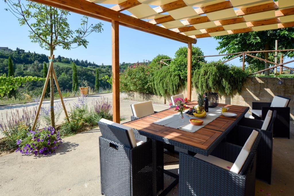 An outdoor patio with a wooden table and wicker chairs, surrounded by greenery and a scenic view.