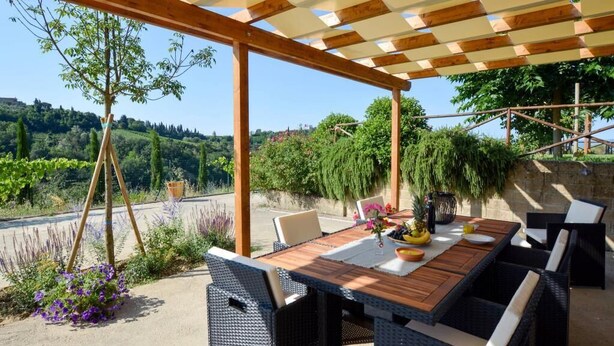 An outdoor patio with a wooden table and wicker chairs, surrounded by greenery and a scenic view. - VILLA CASALE IL BOSCHETTO - JACUZZI & FITNESS & PLAYGROUND OPEN AIR (Certaldo (Firenze))