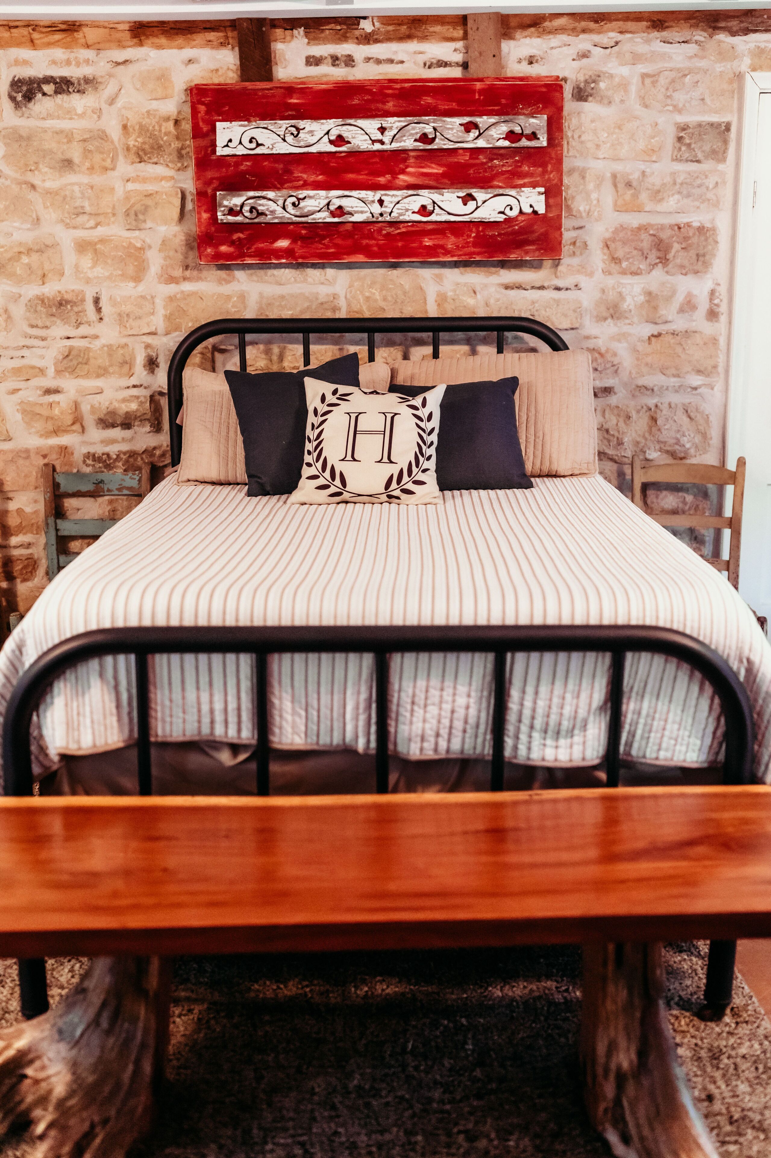 A bed with a striped bedspread, two pillows, and a headboard against a stone wall.
