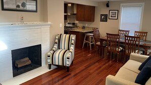 A living room with a fireplace, striped armchair, wooden dining table with chairs, kitchen area, and a framed picture on the wall. - Newly Remodeled! Near Old Town - 2 metros - Solar Home away from home 1600sq (Alexandria)