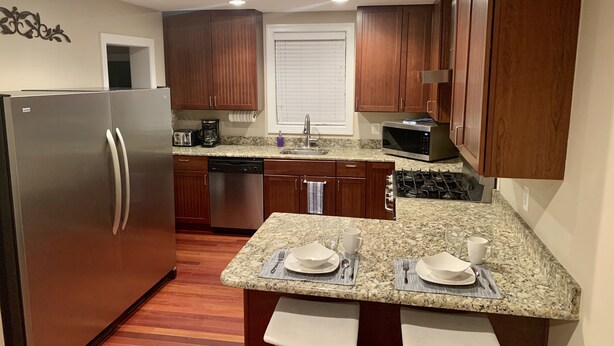 A compact kitchen with wooden cabinets, a stainless steel refrigerator, a microwave, and a gas stove. There is a small island with two stools and a sink. - Newly Remodeled! Near Old Town - 2 metros - Solar Home away from home 1600sq (Alexandria)