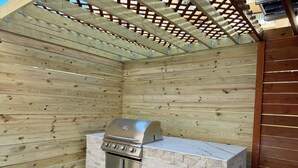 An outdoor kitchen with a built-in grill and stone accents, surrounded by wooden walls and a pergola. - Newly Remodeled! Near Old Town - 2 metros - Solar Home away from home 1600sq (Alexandria)