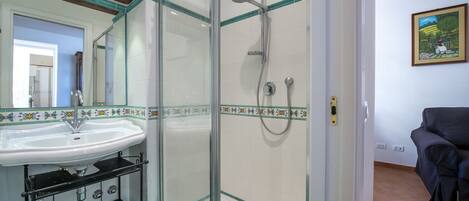 A bathroom with a glass-enclosed shower, a white sink with a black soap dispenser, and a tiled floor.