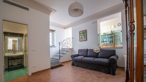 A spacious living area with a staircase, a sofa, and a kitchen area visible in the background. - Casa Cimino A (Praiano)