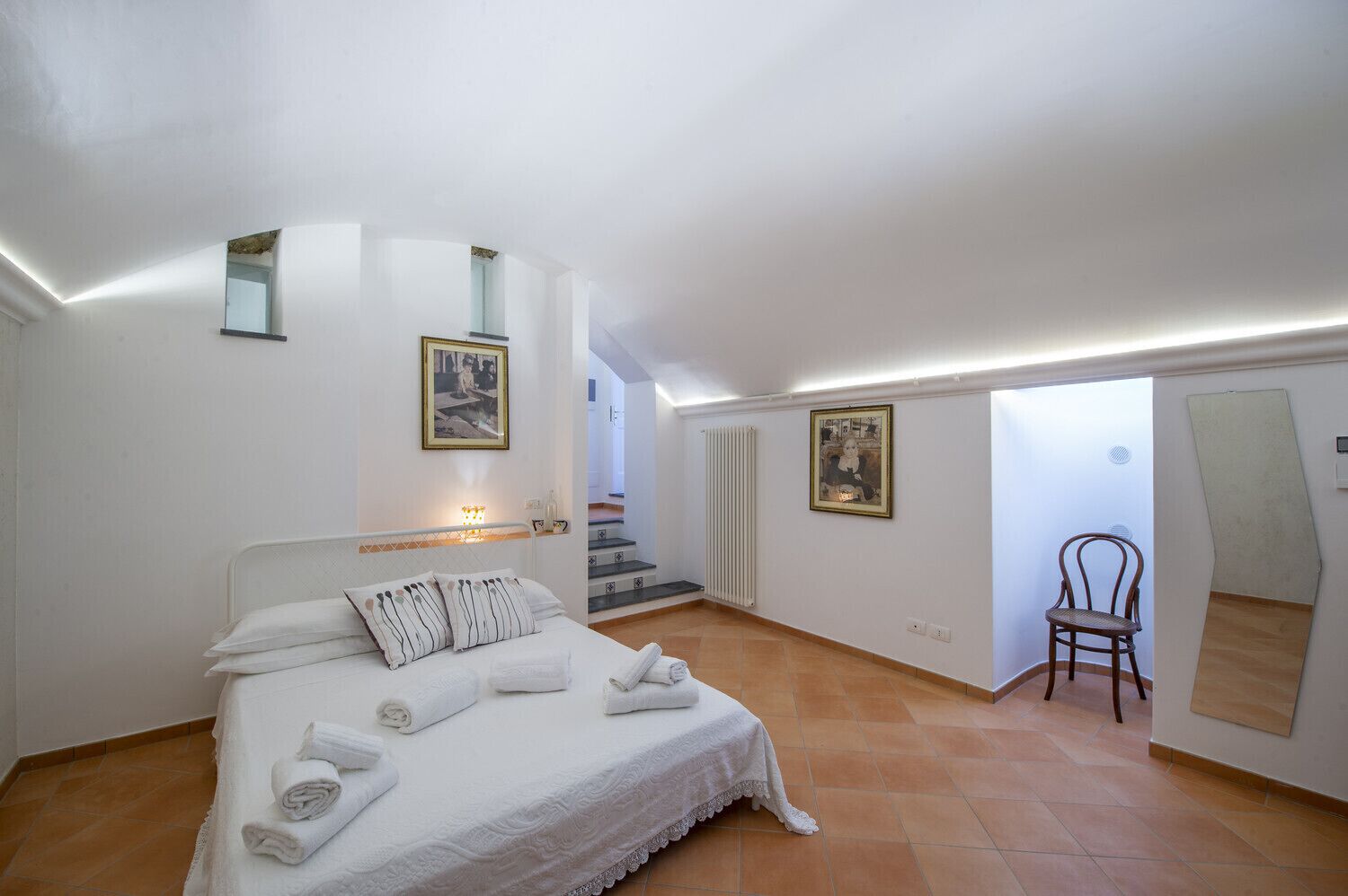 Un dormitorio con una cama grande, dos cuadros en la pared, una silla y una escalera que lleva a otra habitación.