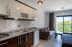 Una cocina moderna con salpicadero de azulejos, electrodomésticos de acero inoxidable y armarios de madera. Hay un comedor con sofá y un balcón con vistas.