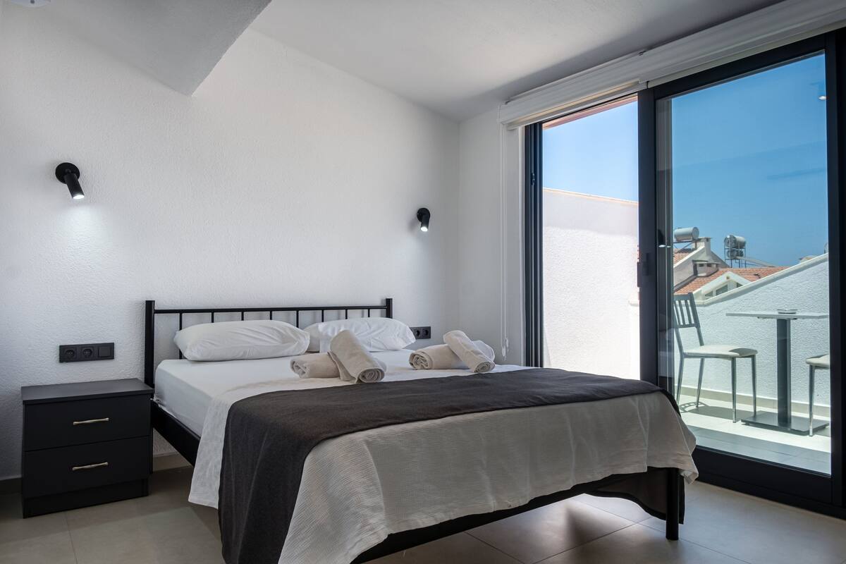 Ein modernes Schlafzimmer mit einem großen Bett, einem Nachttisch und Blick auf den Balkon.