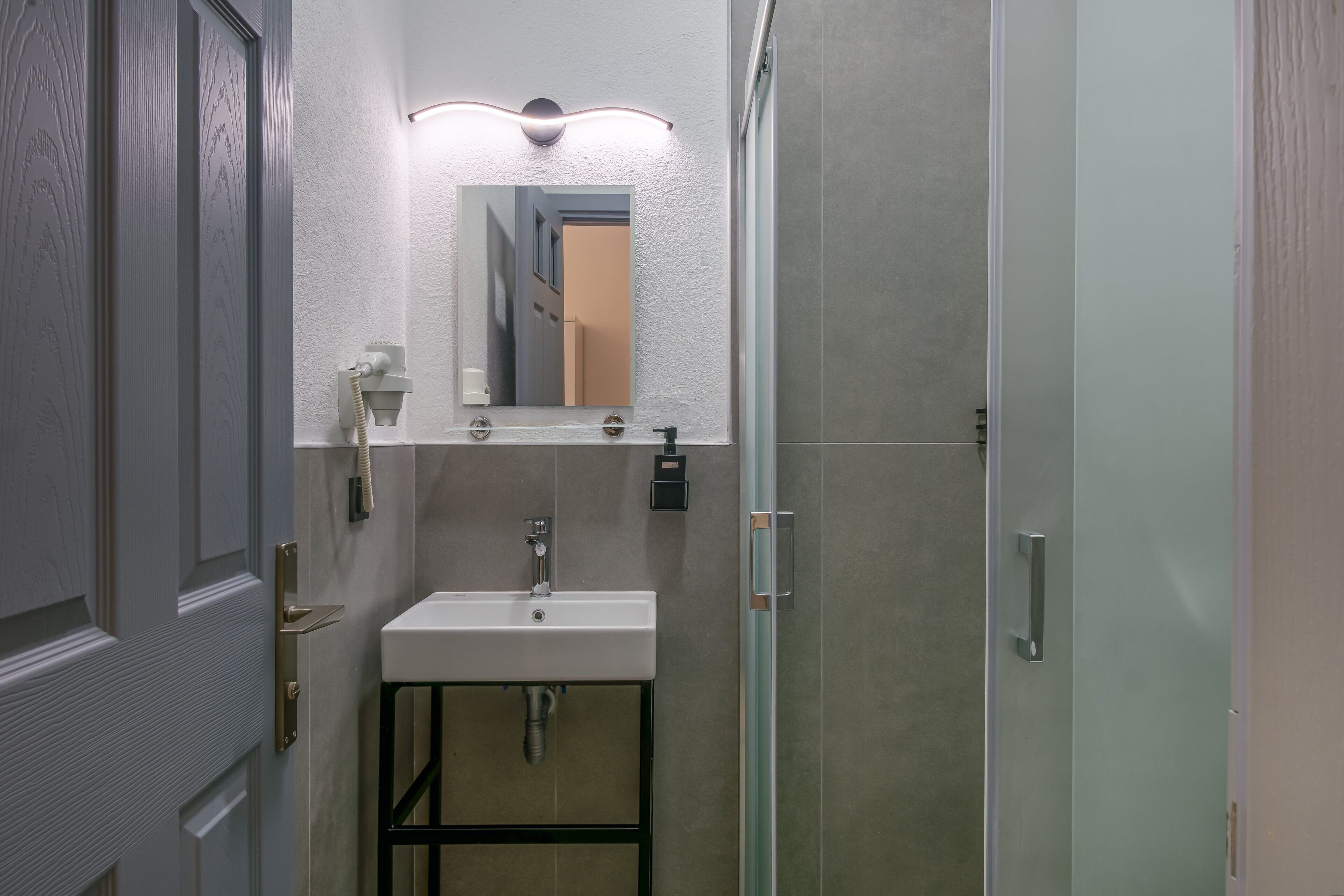 A modern bathroom with a white sink, a mirror above it, and a shower area to the right.