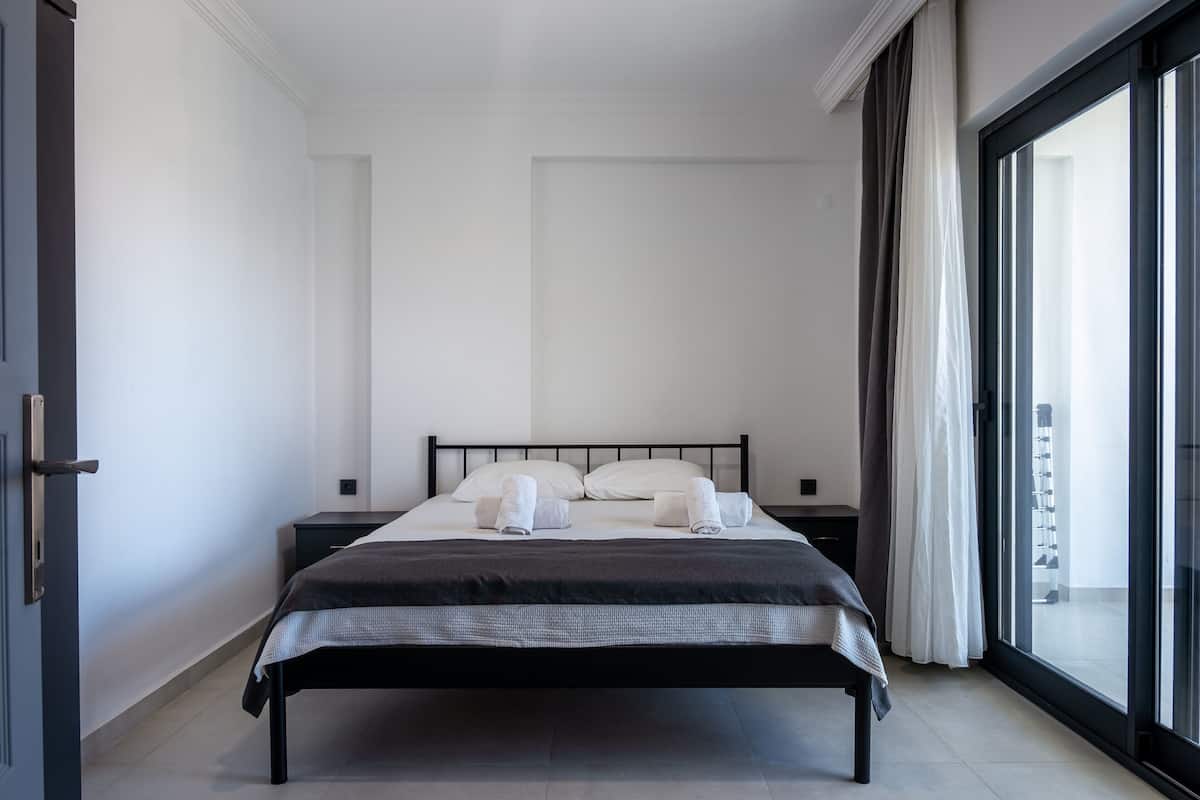 Ein modernes Hotelzimmer mit einem großen Bett, einem Nachttisch und Blick durch eine Schiebetür.