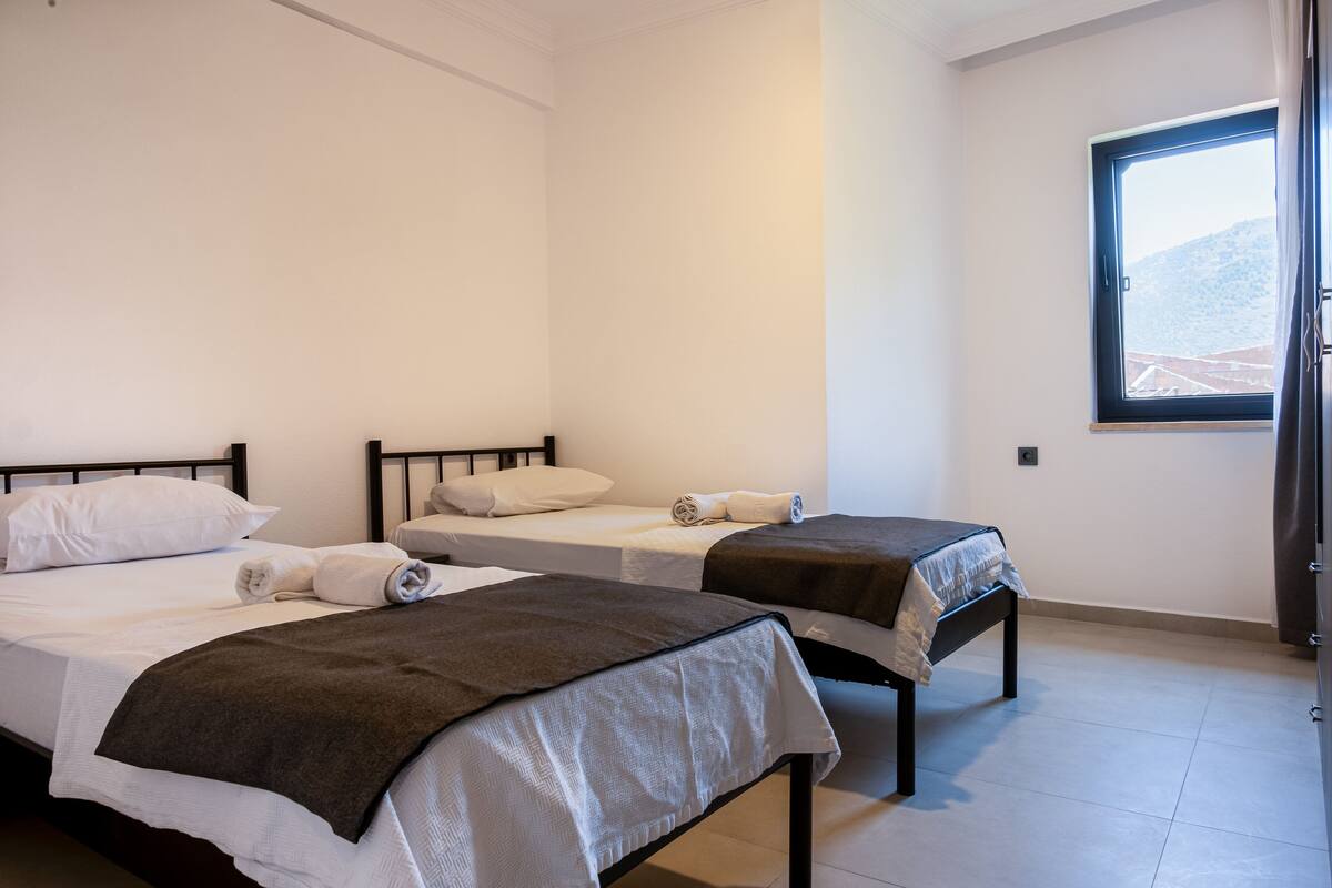 Ein Hotelzimmer mit zwei Einzelbetten, einem Fenster mit Bergblick und einer Tür auf der rechten Seite.