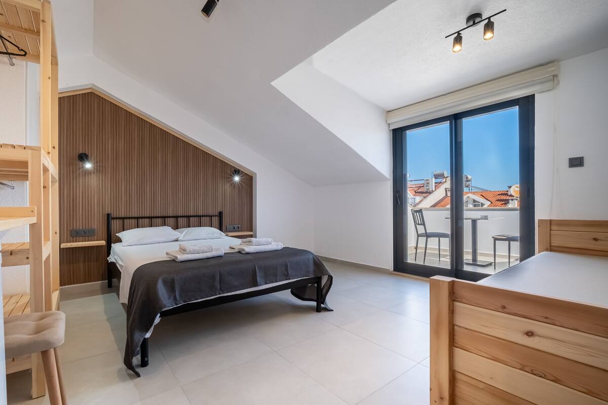 Ein modernes Schlafzimmer mit Bett, Holzmöbeln, einem großen Fenster und Blick auf Gebäude.