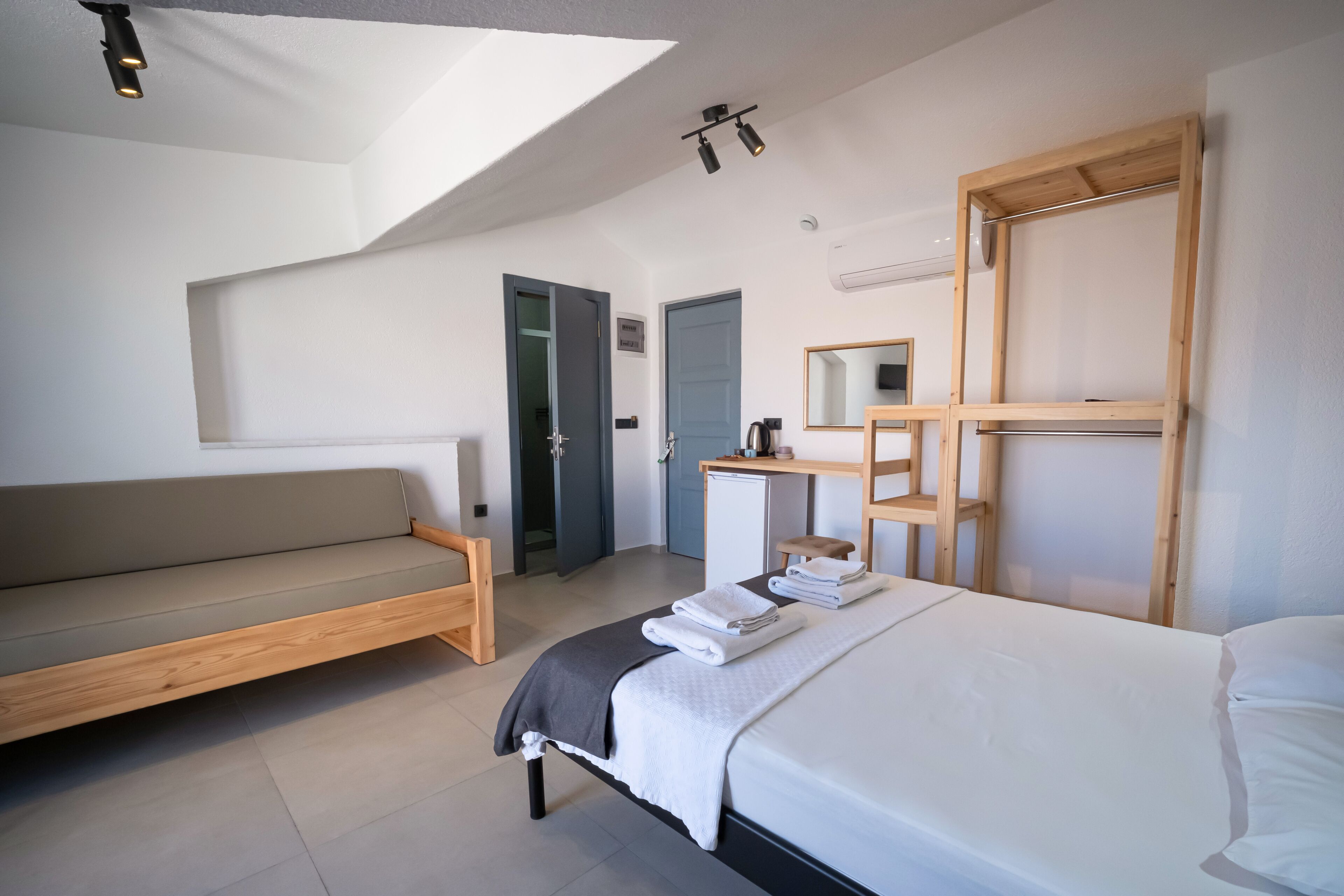 A modern hotel room with a bed, a sofa, a desk, and a mirror.