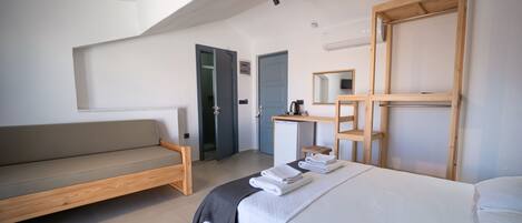 A modern hotel room with a bed, a sofa, a desk, and a mirror.