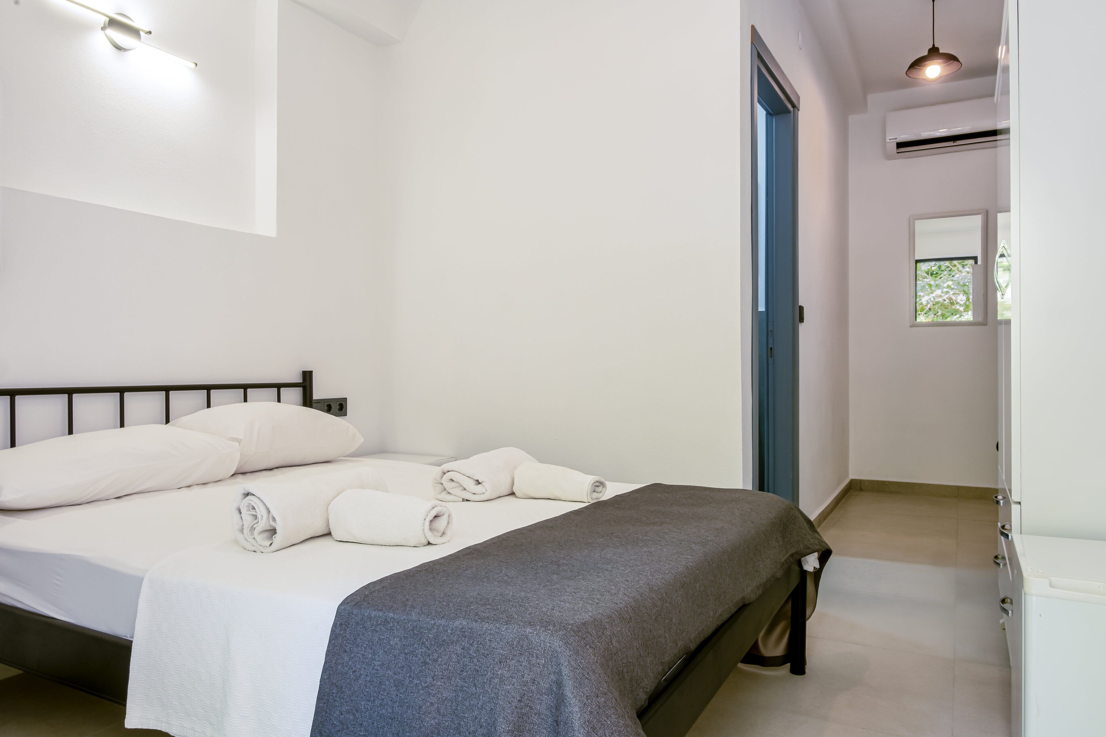 A neatly made bed with white linens and rolled towels, a grey blanket, and a black metal headboard.