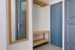 Un pasillo con una puerta azul, un estante de madera y un tendedero colgante.