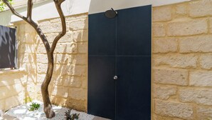 A modern outdoor shower with a black door, a tree, and a stone wall. - 4000 Casa Chiaraluna by Barbarhouse (Porto Cesareo)