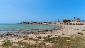 A coastal beach with rocky shoreline, clear blue water, and buildings in the background. - 4000 Casa Chiaraluna by Barbarhouse (Porto Cesareo)