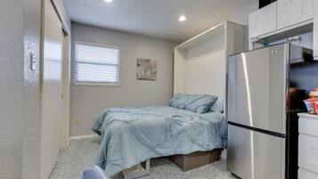 A compact bedroom with a bed, a window, a refrigerator, and a small kitchenette.