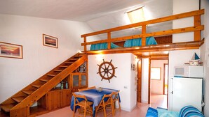 A room with a bunk bed, wooden staircase, a dining table with chairs, a ship's wheel decoration, and a refrigerator. - Fantastic Sardinia casa capitano CAP01 (Budoni)