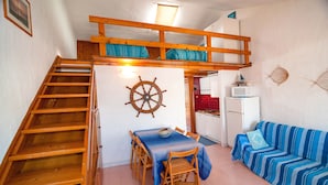 A compact living space with a wooden staircase, a dining area with a table and chairs, a striped sofa, and a kitchen area with a microwave. - Fantastic Sardinia casa capitano CAP01 (Budoni)