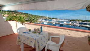 A terrace with a table and chairs, overlooking a marina with boats and a hillside in the background. - Fantastic Sardinia casa capitano CAP01 (Budoni)