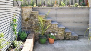Un mur de pierre avec des marches menant à une clôture en bois, le tout entouré de plantes en pot et d’un espace aménagé en jardin.