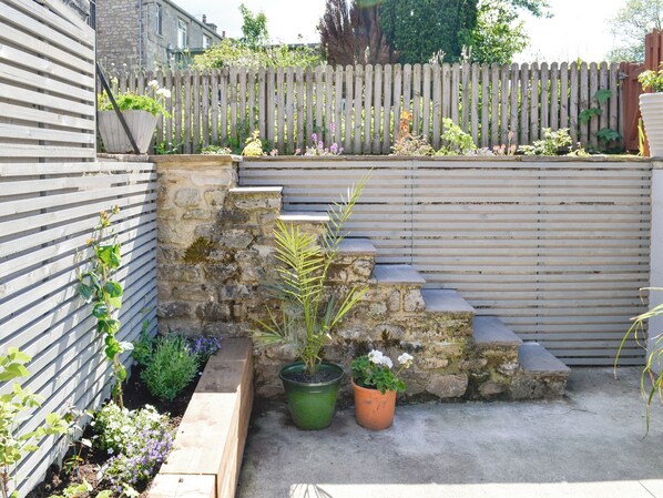 Un mur de pierre avec des marches menant à une clôture en bois, le tout entouré de plantes en pot et d’un espace aménagé en jardin.