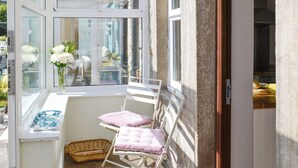 Une pièce baignée de lumière, avec une fenêtre, une chaise, une petite table sur laquelle est posé un vase de fleurs et un panier en osier.