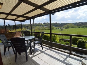 A covered outdoor seating area with a table and chairs, overlooking a green landscape with fields and trees. - Comfortable Chalet in Petithan With Garden (Durbuy)