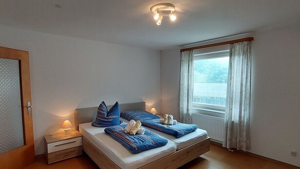 Ein Schlafzimmer mit Bett, Nachttischen, einem Fenster mit Vorhängen und einer Deckenleuchte.