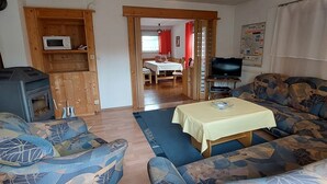 Ein Wohnzimmer mit einer Sofagarnitur, einem Tisch, einem Fernseher und einem Kaminofen.