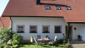 Ein Haus mit rotem Ziegeldach, weißem Anstrich und einem kleinen Garten mit Tisch und Stühlen.