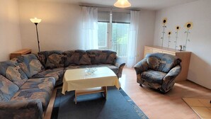 Ein Wohnzimmer mit Ecksofa, einem Sessel, einem kleinen Tisch und einer Deckenleuchte.
