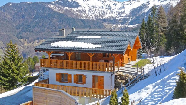 Un chalet doté d’un balcon, d’un toit enneigé et surplombant un paysage montagneux.