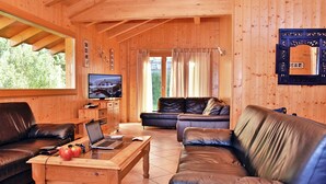 L’intérieur d’un chalet en bois présente un salon avec deux canapés en cuir, une table basse sur laquelle se trouve un ordinateur portable et un téléviseur fixé au mur.