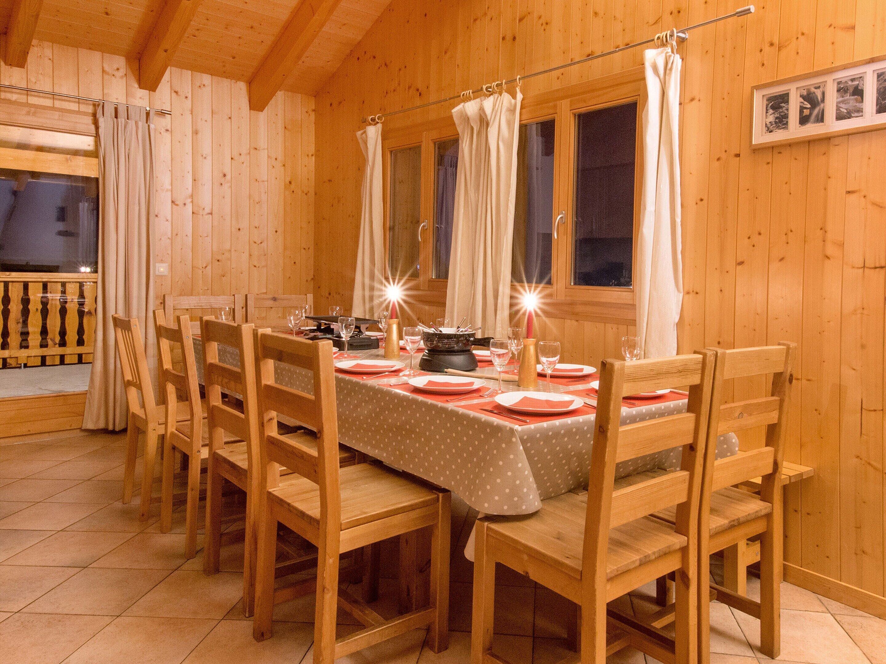 A wooden dining room with a table set for four, chairs, and curtains.