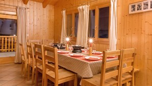 Une salle à manger en bois avec une table dressée pour quatre personnes, des chaises et des rideaux.