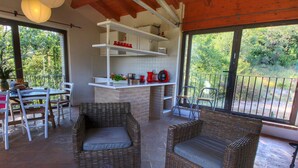 A covered outdoor dining area with wicker furniture, a bar counter, and a view of the surrounding greenery. - Holiday Home With Pool Near Assisi (Assisi)