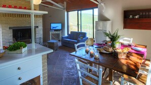 A cozy living area with a fireplace, a television, a dining table with food, and a balcony with a view. - Holiday Home With Pool Near Assisi (Assisi)