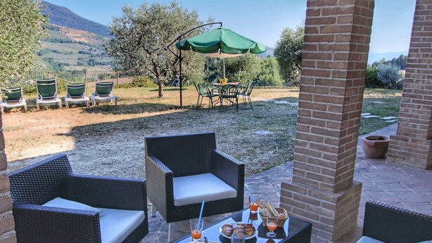 An outdoor patio with wicker furniture, a table set with food and drinks, and a green umbrella. - Holiday Home With Pool Near Assisi (Assisi)