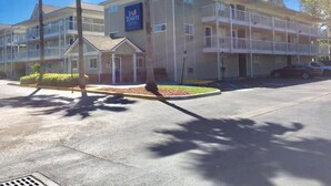 A multi-story hotel with balconies, a sign indicating it's an In Town Suites hotel, and a parking lot with a palm tree and shrubbery. - InTown Suites Extended Stay Jacksonville FL - St. Johns Bluff Rd (Jacksonville)
