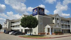 Un hôtel avec une enseigne indiquant « In Town Suites », doté d’un design moderne, de plusieurs étages et d’une entrée couverte.