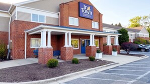 A brick building with a sign reading 'In Town Suites.' It has a covered entrance with columns, a blue door, and a parking lot with cars. - InTown Suites Extended Stay Chicago IL - Oakbrook  (Villa Park)