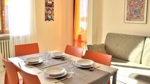 A dining area with a table set for four, orange chairs, and a grey sofa in the background. - Holiday Home in Lazise Near Lake Garda (Lazise)
