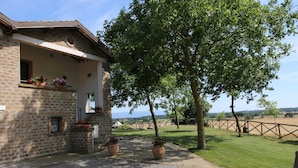 Un bâtiment rustique en pierre, doté d’un porche, de plantes en pot et offrant une vue sur la campagne.