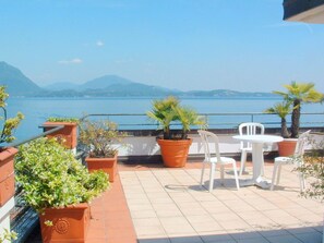 Une terrasse agrémentée de plantes en pot, de chaises blanches et offrant une vue sur un lac et des montagnes.
