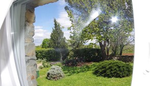 Vista a través de una ventana con marco de piedra, un césped cuidado y una variedad de árboles y arbustos.